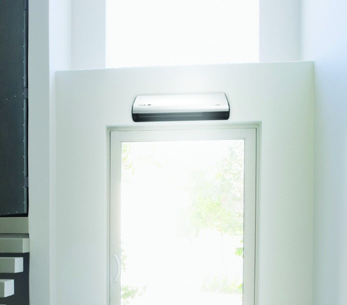 ATC Welcome over door heater mounted on the wall above a glazed door in a bright white room.