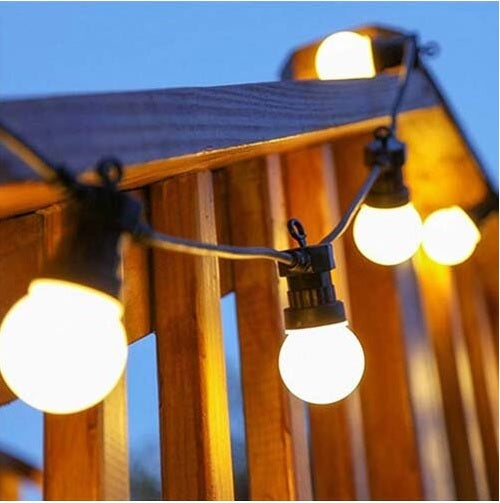 10m opal warm white LED festoon lights glowing on a wooden railing outdoors