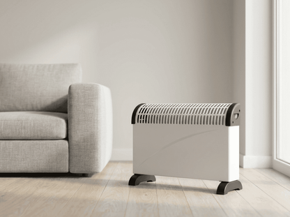 A white Titan 2kW convector heater standing on its black feet on a pale oak floor beside a light grey sofa in a bright Irish living room