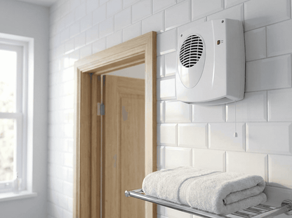 A white Titan downflow bathroom heater mounted high on a white tiled wall above a doorway, with its pull cord hanging down and folded towels on a rail below