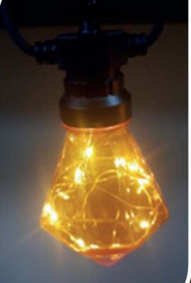 Yuletide amber diamond festoon lamp lit, a diamond shaped amber lens with fine LED wire inside on a black holder